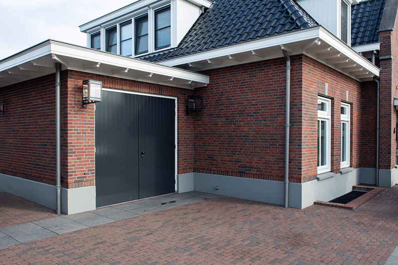 Een moderne bakstenen woning met een donkergrijze garagedeur, ramen met witte kozijnen en een strak betegelde oprit onder een pannendak.