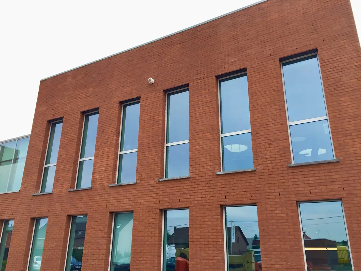 Een modern bakstenen gebouw met twee verdiepingen, met hoge rechthoekige ramen waarin de lucht en de nabijgelegen gebouwen weerspiegelen.