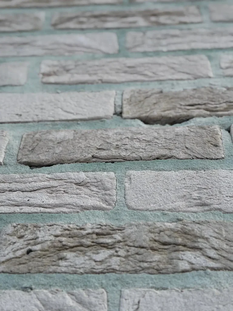 Close-up van een stenen muur met lichtgrijze stenen en zichtbare ruwe texturen, gescheiden door groenachtige mortel.